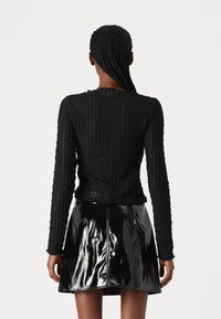 Black textured knit long-sleeve top paired with a shiny black patent leather mini skirt. Features ribbed details and a fitted silhouette.