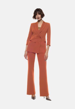 Blazer arancione doppiopetto con revers, abbinato a pantaloni a palazzo coordinati. Tessuto liscio con vestibilità sartoriale.