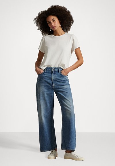 Lys grå bomulls T-skjorte med korte ermer, kombinert med vide blå denimjeans. Jeansene har en falmet vask og en klassisk knappefront.