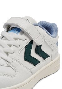 Biała trampka z teksturowaną skórzaną cholewką, zdobiona zielonymi zygzakowatymi akcentami, niebieską siateczkową podszewką oraz zapięciem na rzep.