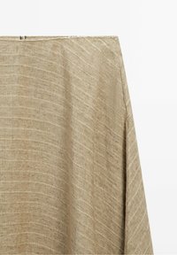 Tissu beige tissé avec de subtiles rayures diagonales et une couture visible sur le côté droit, suspendu sur un fond blanc.