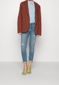 Brun oversized blazer, ljusblå skjorta med knappar, slitna ljusblå jeans och gröna sandaler med remmar.