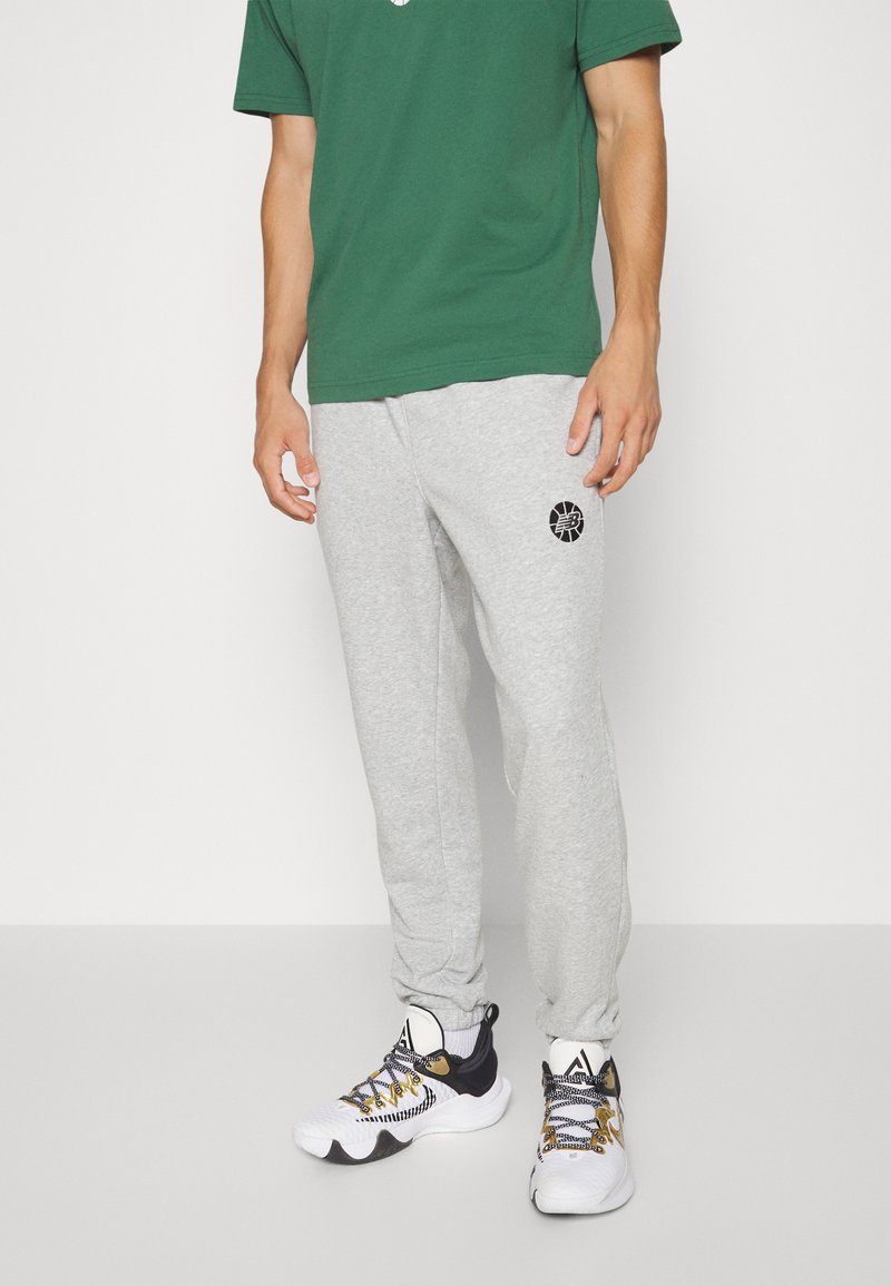 Graue Jogginghosen mit einem schwarzen Logo, kombiniert mit einem grünen T-Shirt und schwarz-weißen Sportschuhen mit gelben Akzenten.