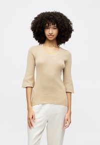 Beige Strickoberteil mit Rundhalsausschnitt, Dreiviertelärmeln und Rippstruktur, kombiniert mit leichten, locker sitzenden Hosen.