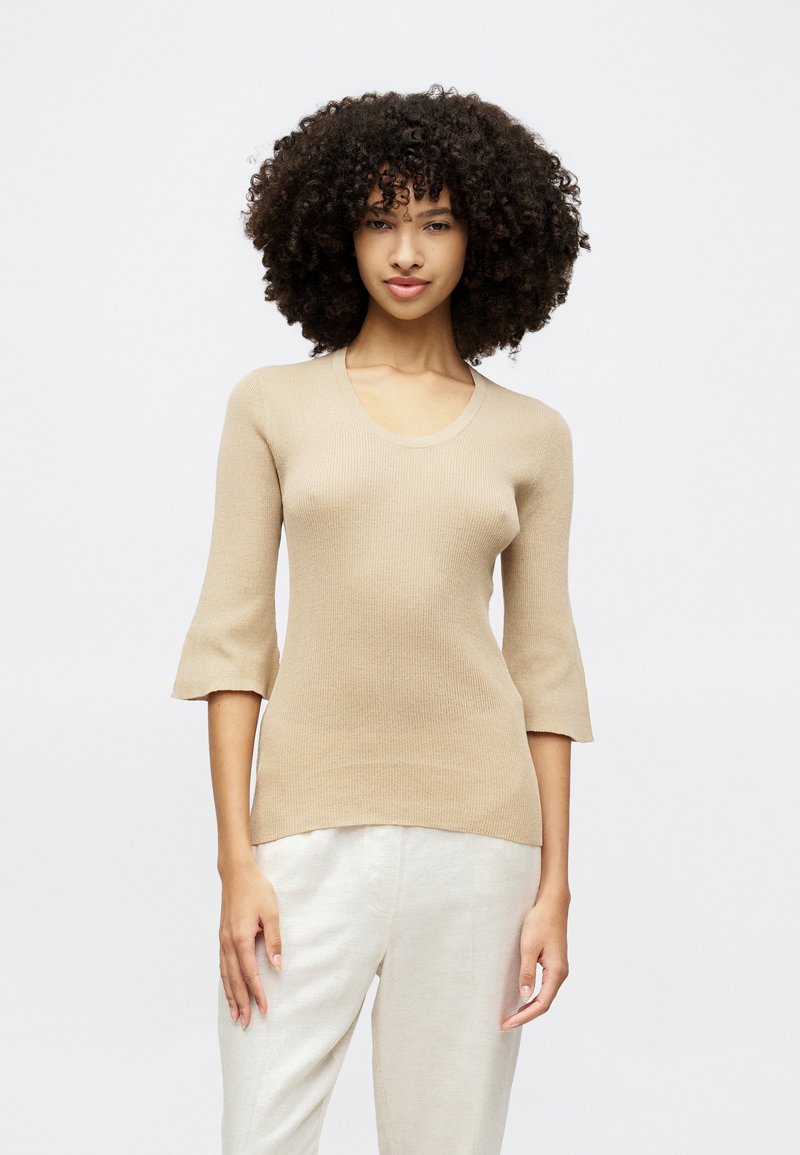 Beige Strickoberteil mit Rundhalsausschnitt, Dreiviertelärmeln und Rippstruktur, kombiniert mit leichten, locker sitzenden Hosen.