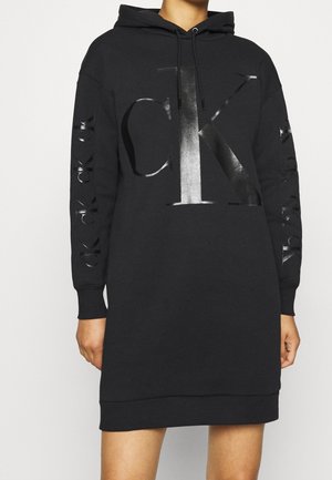 Robe à capuche noire à manches longues avec un grand logo "CK" brillant sur le devant et de petits logos "ck" courant le long des deux manches.