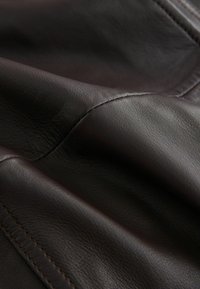 Dunkelbraunes Ledergewebe mit glatter Textur, sichtbar genähten Nähten und sanften Falten. Keine auffälligen Muster oder Hardware-Details.