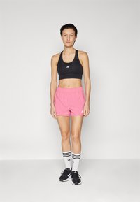 Sujetă sport neagră, pantaloni scurți roz cu talie elastică, încălțăminte neagră și șosete albe cu trei dungi negre. Design athletic simplu.