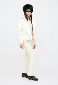 White waterproof jacket and pants, black faux fur hat, black sunglasses, and chunky heeled black boots with chain accents.