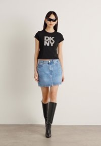 Schwarzes, enganliegendes T-Shirt mit glitzerndem "DKNY"-Schriftzug, kombiniert mit einem blauen Denim-Minirock und schwarzen kniehohen Stiefeln. Schlichtes Design, lässiger Look.