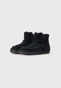 Botas de tobillo de ante negro con una textura suave, puntera redondeada y detalles de costura alrededor de la suela. Presentan un diseño de doblez.