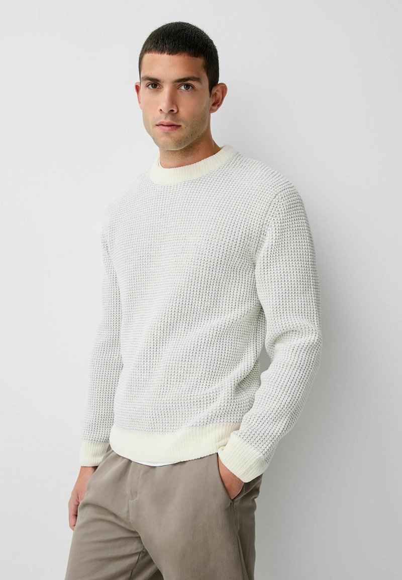 Pulover alb din tricot cu un model texturat, guler rotund cu nervuri și manșete. Purtați cu pantaloni de culoare deschisă.