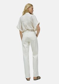 Jeans blancos de tiro alto con pierna recta, combinados con una camisa de crema de manga corta y textura, y sandalias beige.