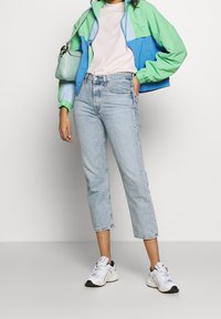 Färgglad jacka i grönt och blått, vit t-shirt, ljusblå cropped jeans och vita sneakers med svarta detaljer. Liten ljusgrön handväska.