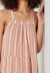 Abito con stampa floreale e spalline larghe, caratterizzato da righe orizzontali rosse e beige. Tessuto leggero, vestibilità ampia, corpetto plissettato.