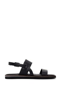 Black leather sandal featuring a flat sole, interwoven strap design, adjustable ankle buckle, and minimalistic silhouette.