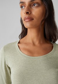 Hellgrünes Langarmoberteil mit einem runden Ausschnitt, aus weichem geripptem Stoff gefertigt. Einfaches Design ohne Verzierungen.