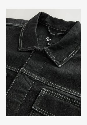 Sort denimjakke med kontrastfarvet hvid syning, krave og brystlommer, med en struktureret stofoverflade.