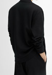 Zwarte sweatshirt met lange mouwen, geribbelde manchetten en een ronde hals. Zacht materiaal, relaxte pasvorm en minimalistisch ontwerp. Geen zichtbare branding.