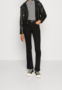 Musta nahkainen moottoripyörätakki mustavalkoisen raitaiseen poolopaitaan, yhdistettynä korkeavyötäröisiin mustiin levennettyihin housuihin ja mustiin tennareihin.