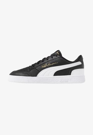 Sneaker Puma basse noir et blanc avec semelle blanche, lacets noirs, bande signature et texte doré "Ralph Sampson" sur le côté.