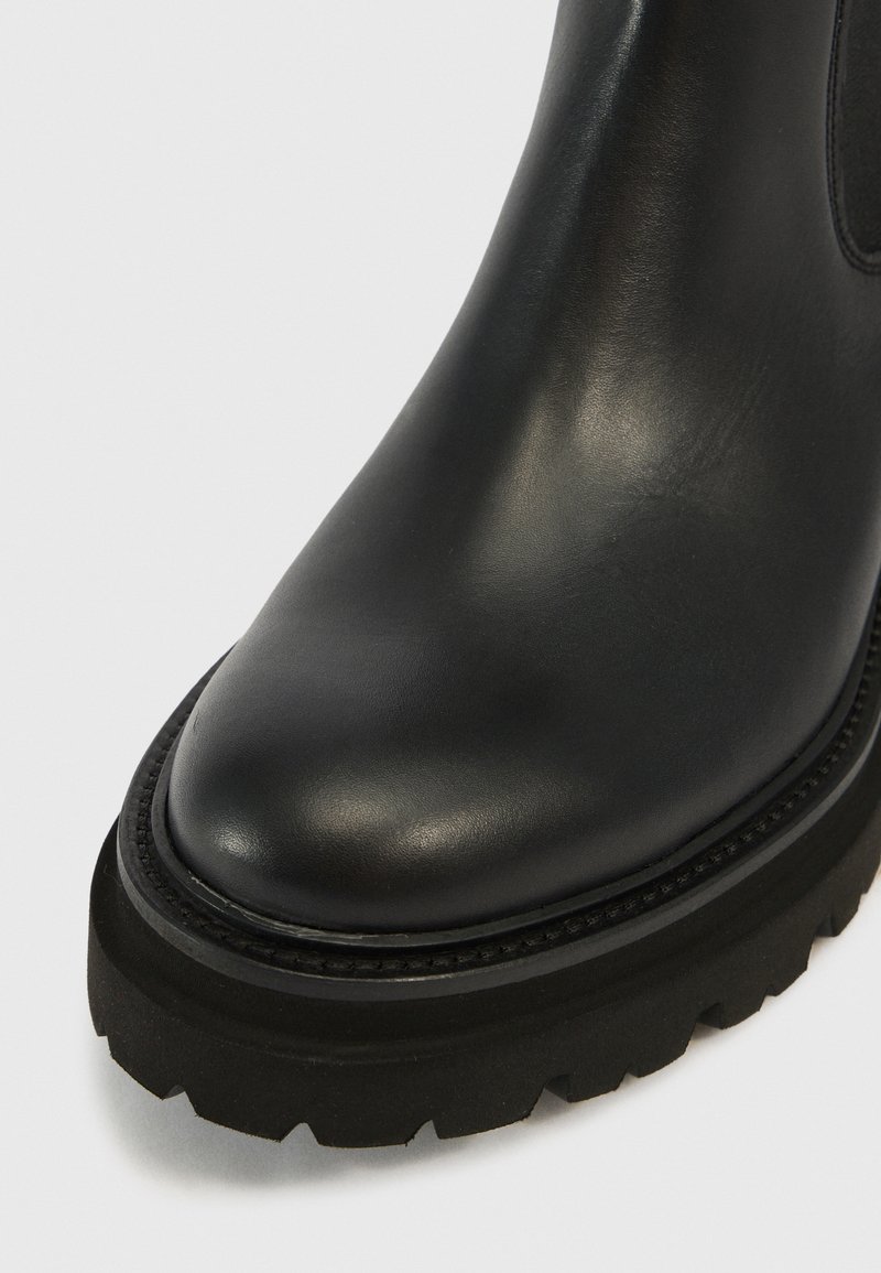 Botte en cuir noir à bout rond et semelle en caoutchouc épaisse et texturée présentée en gros plan sur un fond blanc.