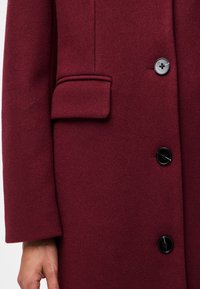 Μπουφάν από μαλλί σε βουργουνδί χρώμα με γιακά notch, μια τσέπη στο στήθος και μαύρα κουμπιά μπροστά. Ομαλή υφή με εφαρμοστή γραμμή.