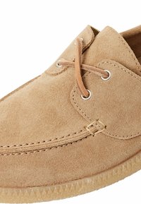 Beige Wildlederschuh mit runder Spitze, zwei Ösen, braunen Schnürsenkeln und einer strukturierten Sohle. Besitzt minimale Nähte und ein klares Design.