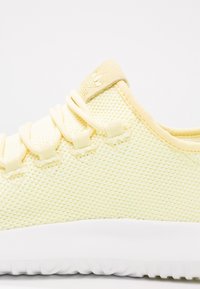 Gul nät sneakers med en texturerad ovandel, elastiska snören och en vit gummisula. Diskret logotyp nära hälen.