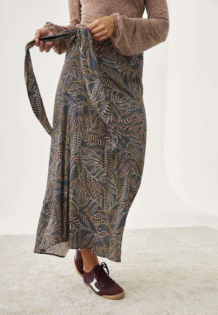 Larga falda fluida con un fondo azul oscuro y patrones intrincados de hojas en verde, amarillo y burdeos. Se ajusta en la cintura con lazos.