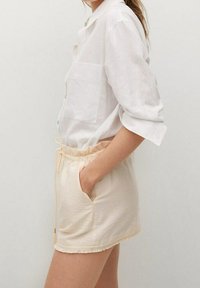 Chemise légère en lin blanc, dotée d'une poche avant, associée à un short crème avec une taille élastique et un ourlet à franges.