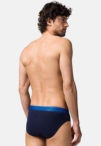 Granatowe bawełniane slipy z niebieskim elastycznym pasem, na którym znajduje się logo. Ubranie ma klasyczny krój i gładką teksturę.