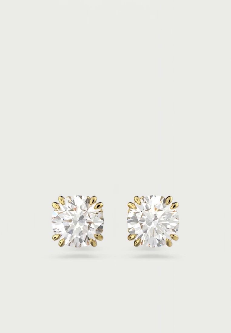 Une paire de boucles d’oreilles puces ornées de pierres rondes, transparentes et facettées, chacune maintenue par des griffes dorées, sur un fond clair.