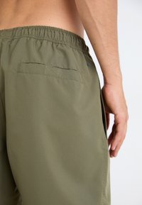 Grønne shorts med elastisk linning, sidelommer og en baklomme. Materialet virker glatt og lett, passende for hverdagsbruk.
