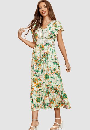 Mujer con un vestido midi blanco con estampado floral, mangas con volantes, detalle de encaje en la cintura y sandalias blancas de tacón ancho con tiras.