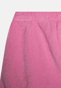 Rosa frotté-stoff med en myk, teksturert overflate. Har en elastisk midje og lett rynke i livet for passform.