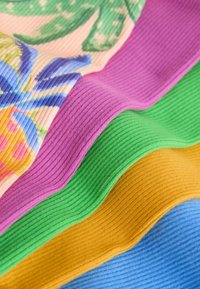 Gros plan sur un tissu côtelé avec des rayures violettes, vertes, jaunes et bleues ainsi qu’un motif floral, présenté en couches douces et pliées.