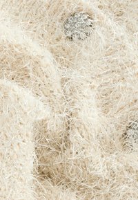 Textured cream knitted fabric with soft, fuzzy strands. Features a decorative silver-toned button with multiple small clear accents.