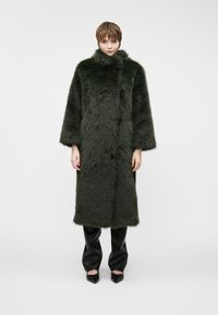 Długi, ciemnozielony futrzany płaszcz z wysokim kołnierzem, szerokimi r�ękawami i gładką teksturą. Noszony na czarnych skórzanych spodniach oraz spiczastych czarnych butach.