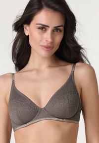 Donna con capelli lunghi e scuri che indossa un reggiseno grigio a fantasia con spalline sottili e leggeri accenti luccicanti, in posa contro uno sfondo chiaro e semplice.