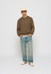 Brun strikkegenser med rillet hals, lyseblå avslappede jeans og beige caps. Skoene har et teksturert design med striper.