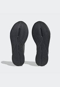 Černé sportovní boty se podrážkami z texturované gumy s diagonálními a vertikálními drážkami pro trakci a odolnost, označené "ADIDAS."