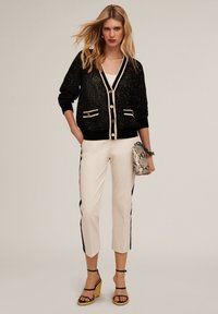 Cardigan nero con paillettes e accenti crema, top bianco, pantaloni cropped crema con strisce laterali nere e borsa a fantasia pitone.