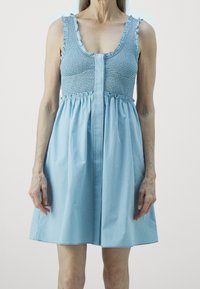 Light blue sundress with smocked bodice and ruffled straps, featuring a flared skirt and a button-down front detail. Cotton fabric.