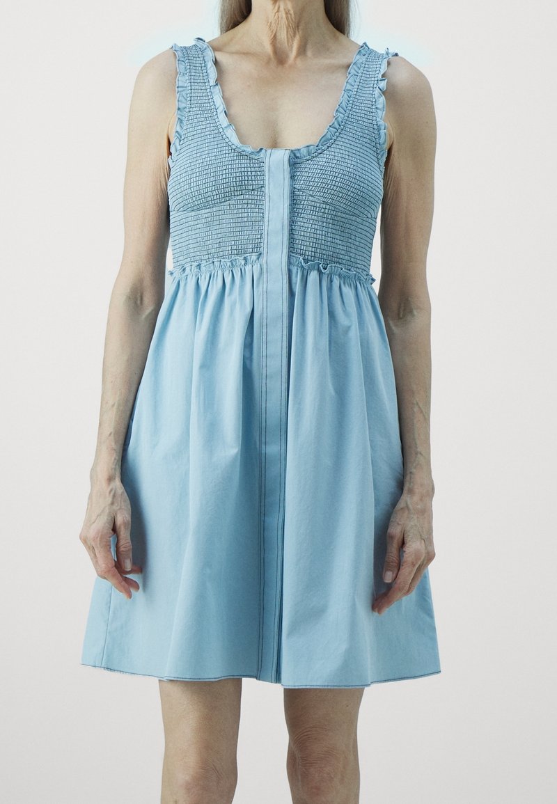Light blue sundress with smocked bodice and ruffled straps, featuring a flared skirt and a button-down front detail. Cotton fabric.