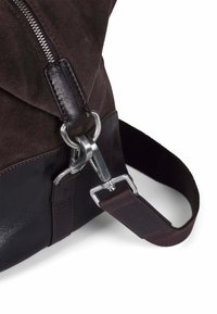 Brun semsket bag med en teksturert overdel, glatt lærbase, sølvfarget hardware og en justerbar stropp med lærdetaljer.