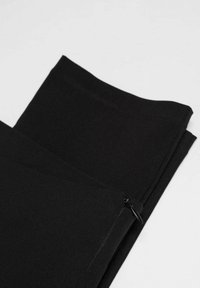 Leggings noirs en tissu extensible, avec une texture lisse et un petit zip sur le côté pour la fermeture.