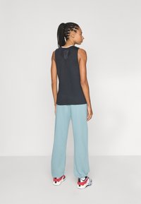 Top nero senza maniche con un dettaglio a taglio sulla schiena, abbinato a pantaloni della tuta blu chiaro e scarpe da ginnastica multicolori.