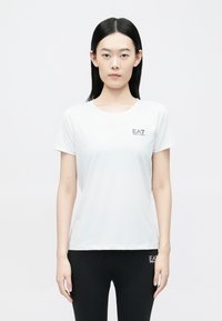 Fehér rövid ujjú póló sima anyagb�ól, bal mellrészen kis fekete EA7 logóval, klasszikus kerek nyakkivágással.
