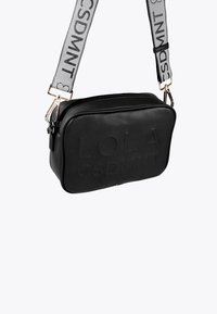 Crni pravokutni crossbody ruksak s utisnutim tekstom "LOLA CSDMNT" i širokim sivo podesivim remenom s crnim natpisom "CSDMNT".